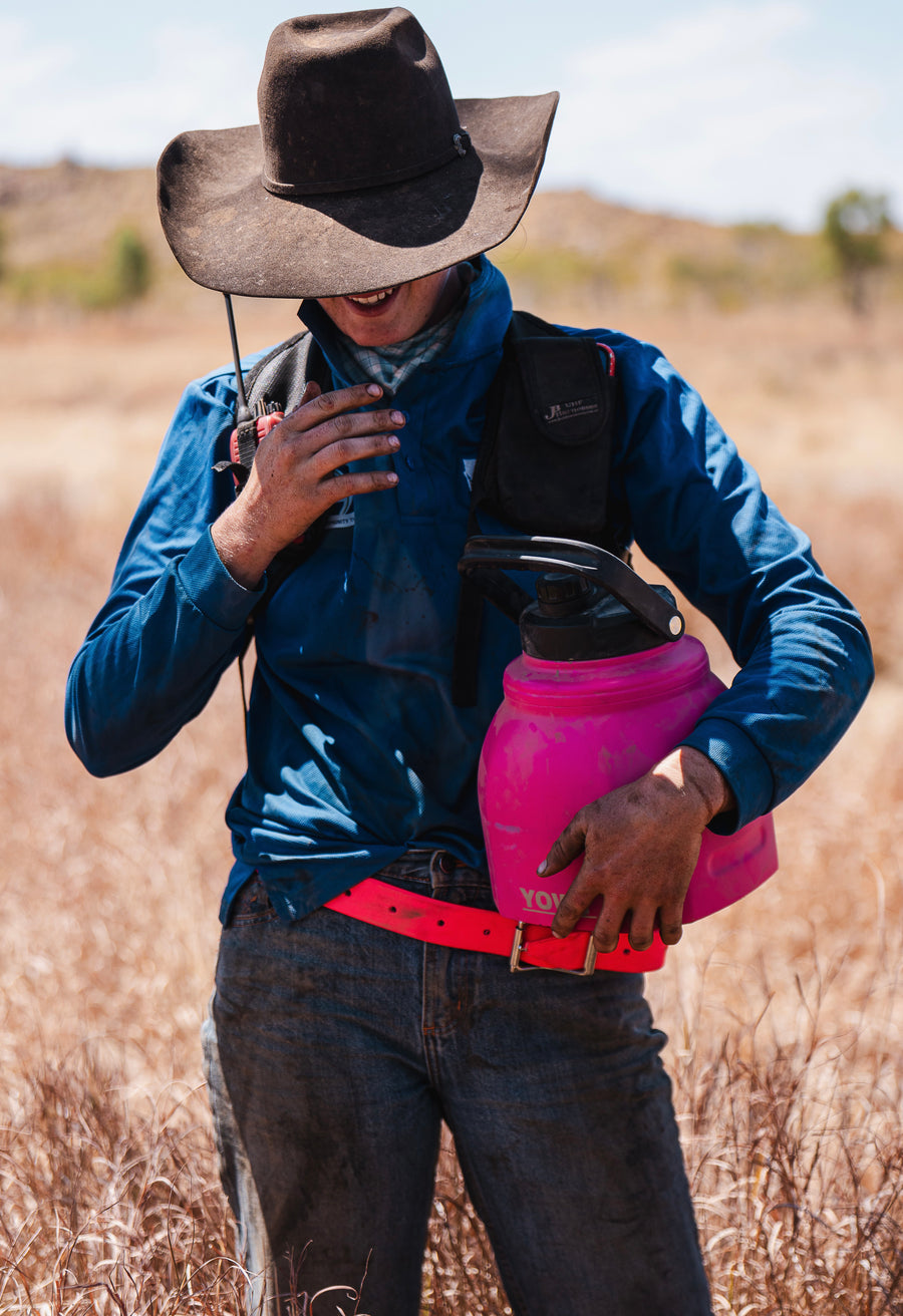 A ringer carrying a pink Yowy watercan through the long grass